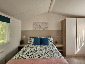 A bedroom with a bed, a window, a radiator, a wall-mounted artwork, and a wooden wardrobe. - Cabin Sleeps 4 to 6 With Parking (Ringwood)