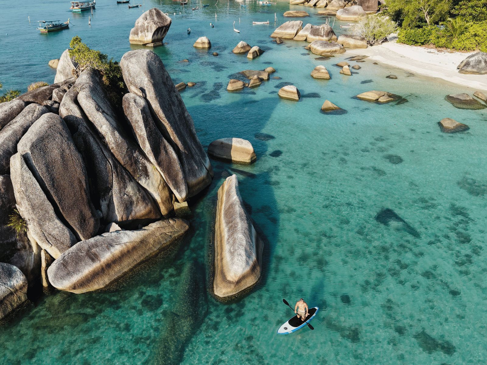 A clear turquoise sea with large rocks and a sandy beach.