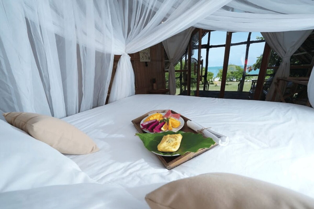 A bed with a canopy, a breakfast tray with fruit and eggs, and a view of the outdoors.