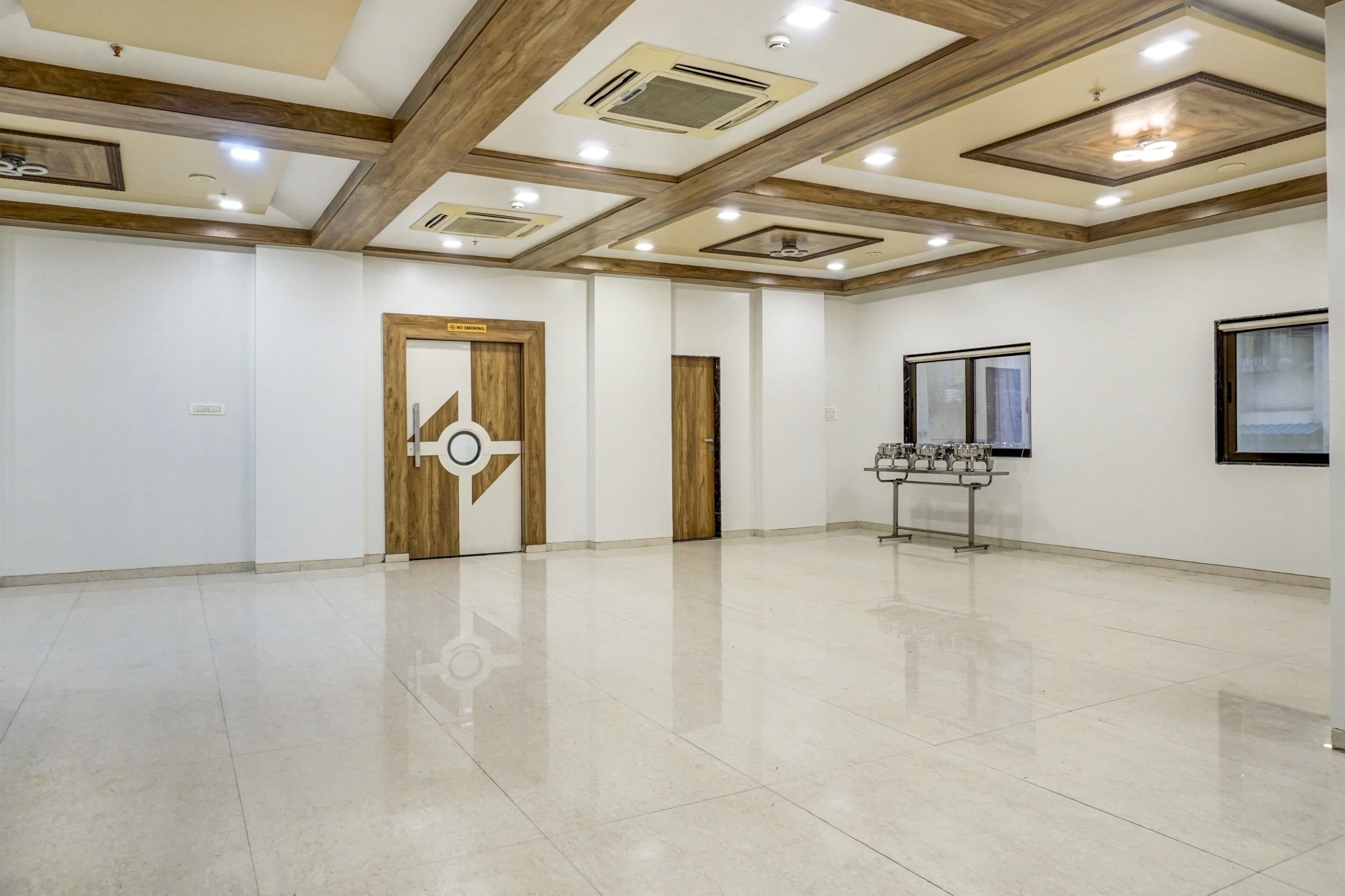 A spacious room with a polished floor, a no-smoking sign, and a window with blinds.