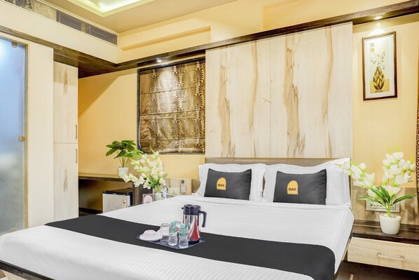 Habitación de hotel con cama, mesitas de noche, calefactor en la pared, una ventana con panel decorativo y un cuadro enmarcado.