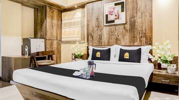 Une chambre d’hôtel avec une tête de lit en bois, un lit avec une literie blanche, une table de chevet avec une lampe, une chaise et un tableau au mur.