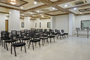 Un salón de conferencias con filas de sillas, una pantalla de proyector y una mesa con equipos.