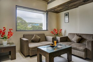 Una sala de estar con dos sofás, una mesa de centro de vidrio y un ventanal con vistas a edificios y árboles.