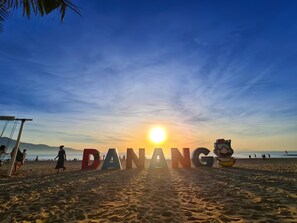 Een strand met grote letters die 'DANANG' spellen en een cartoonpersonage.