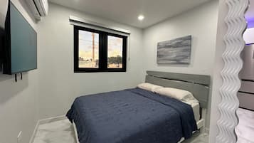 A bedroom with a bed, a window, a wall-mounted air conditioner, and a painting.