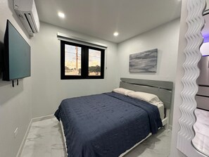 Une chambre à coucher avec un lit, une fenêtre, un climatiseur fixé au mur et un tableau.