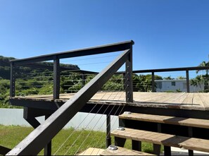 Une terrasse en bois avec une rambarde en métal, donnant sur une pelouse et un ciel dégagé.
