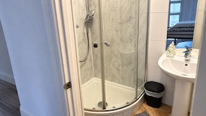 A bathroom with a glass-enclosed shower, a sink with a mirror, and a black trash bin. - Ensuite Studio, Sleeps 4 With Wifi (London)