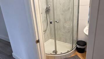 A glass-enclosed shower with a white tiled wall and a small trash bin beside it.