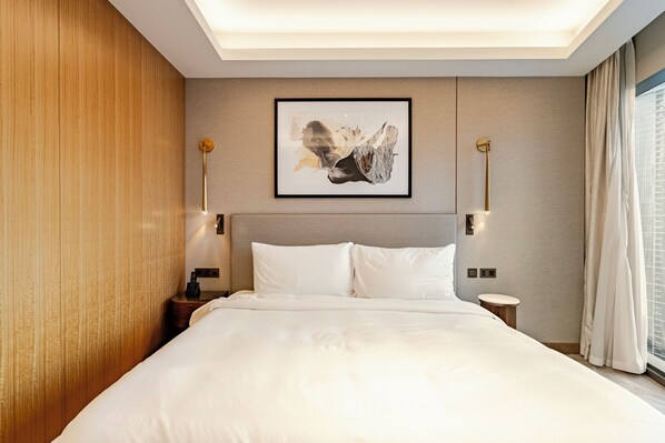 Ein Hotelzimmer mit einem großen Bett, einem Nachttisch, einer Wandleuchte und einem gerahmten Kunstwerk über dem Bett.