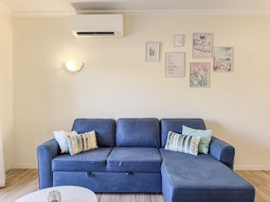 Ein Wohnzimmer mit einem blauen, modularen Sofa, einem runden Couchtisch und einer Wand-Klimaanlage.
