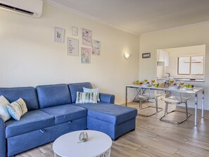 A living room with a blue sofa, a round coffee table, and a dining area with a table and chairs. - #406 Modern 1-Bedroom Apartment with Pool | Near the Oura Strip (Albufeira)