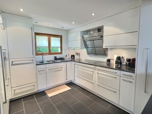 Eine moderne Küche mit weißen Schränken, einem eingebauten Backofen und einem Fenster mit Jalousien.