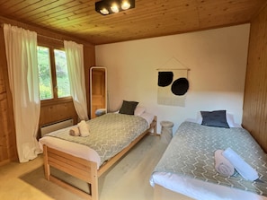 Una habitación con dos camas de madera, una ventana con cortinas, un espejo fijado a la pared y un adorno en la pared.