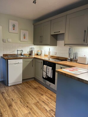 A compact kitchen with a dishwasher, oven, and a wooden countertop. - Charming cottage close to the Cairngorms (Ballindalloch)