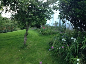 Ein üppiger Garten mit verschiedenen Pflanzen und Blumen, einer gepflegten Rasenfläche und einem Baum in der Mitte.