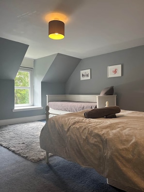 Ein Schlafzimmer mit schrägem Dach, einem Bett mit Kopfteil, einem Fenster und einer Wandleuchte.