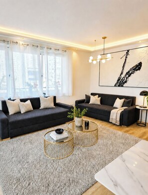 A modern living room with two dark sofas, a glass coffee table, and a large abstract painting on the wall. - R Beautiful newly built apartment near city center (München)