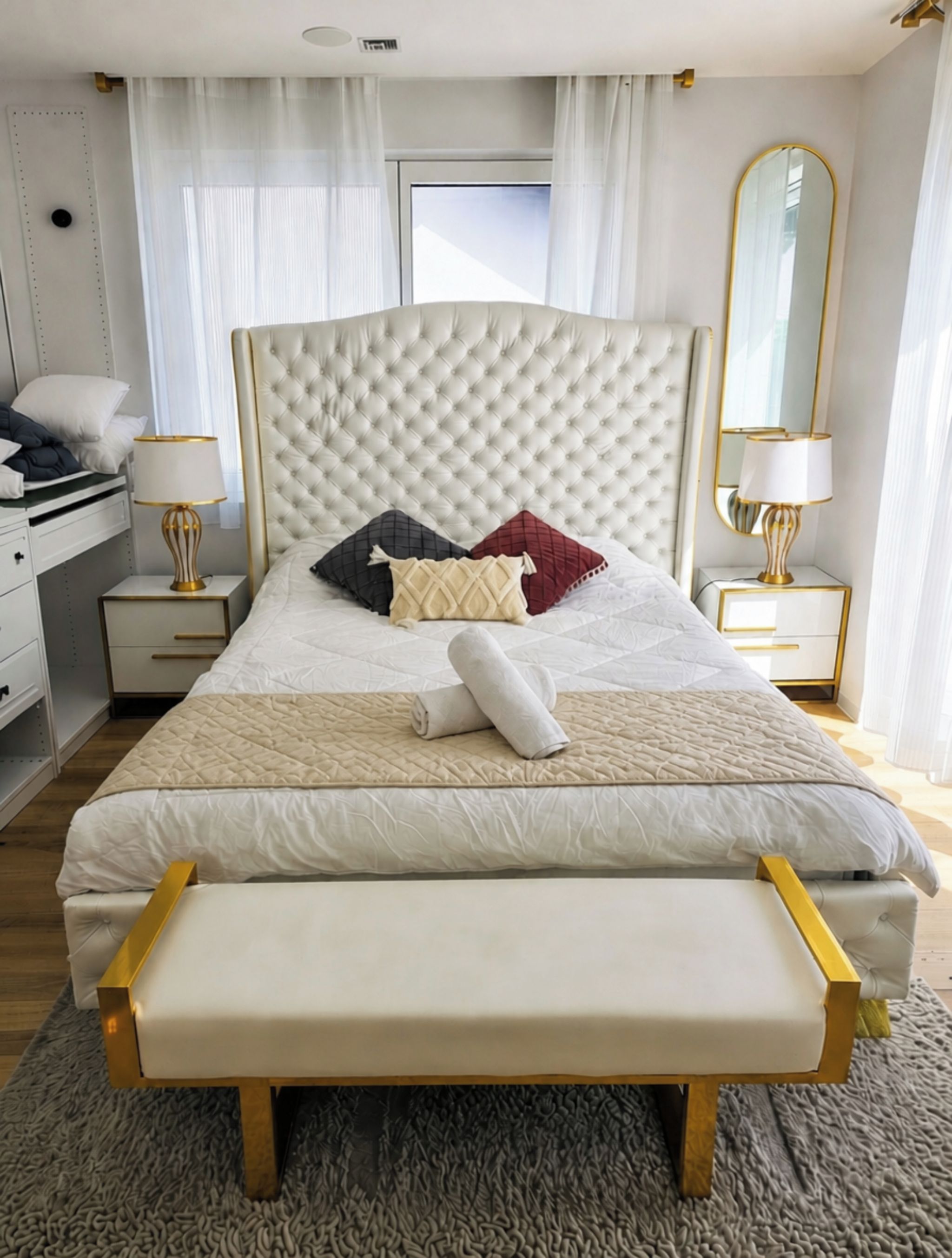 A neatly made bed with a tufted headboard, bedside tables with lamps, and a bench.