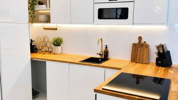 A modern kitchen with white cabinetry, a wooden countertop, a built-in oven, and a sink with a gold faucet.