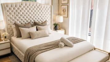 A modern bedroom with a large bed, bedside tables, a bench, and a view of greenery outside.