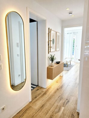 A hallway with a large mirror, a wooden floor, a white door, and a light fixture. - R Beautiful newly built apartment near city center (München)