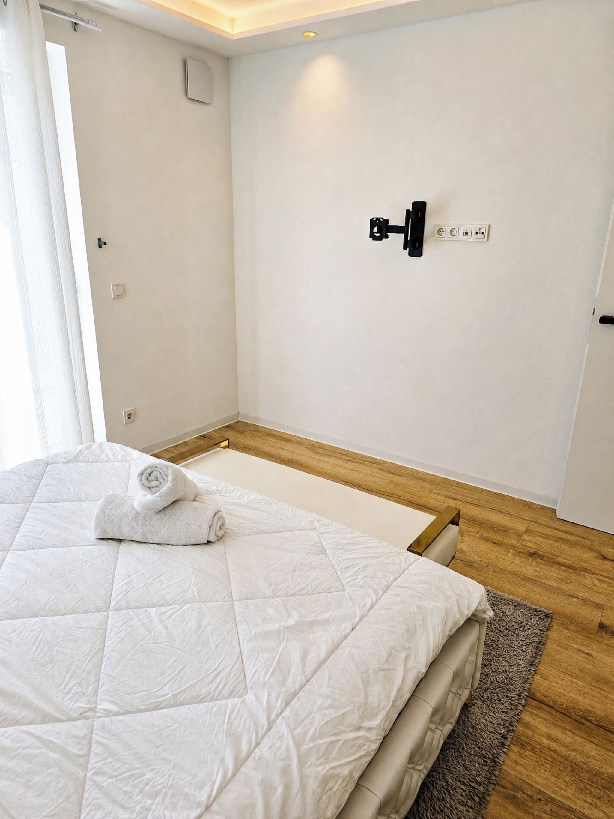 Ett hotellrum med en säng, ett trägolv, en vit vägg och en ljusströmbrytare.