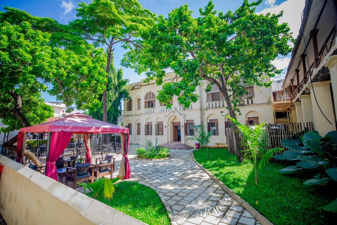 A courtyard with a covered seating area, a pathway, and a building with arched windows.