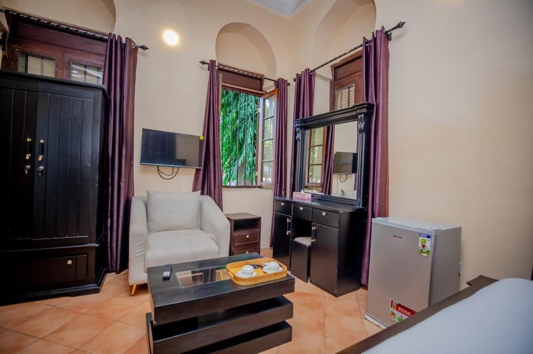 A hotel room with a sofa, a small table with a tray, a desk, a mirror, a television, and a refrigerator.