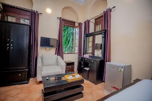Habitación de hotel con sofá, una mesita con bandeja, escritorio, espejo, televisor y refrigerador.