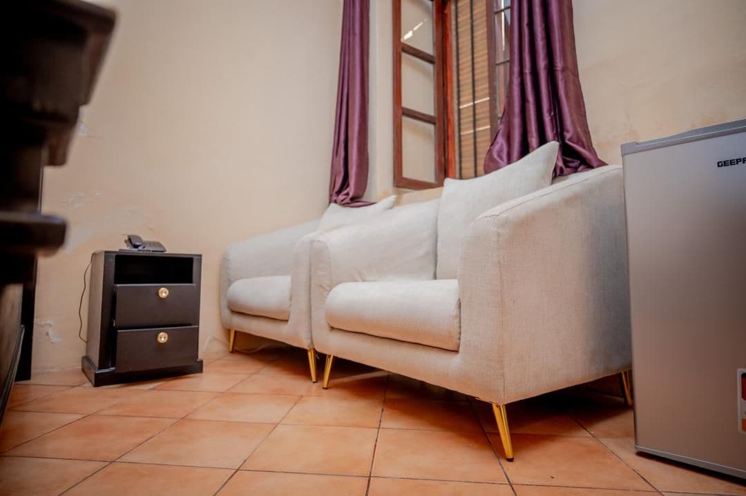A room with a sofa, a small cabinet, and a refrigerator.