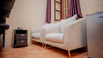 A room with a sofa, a small cabinet, and a refrigerator.