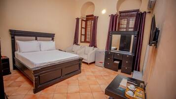 A hotel room with a bed, a sofa, a desk with a tray of breakfast items, and a wardrobe.