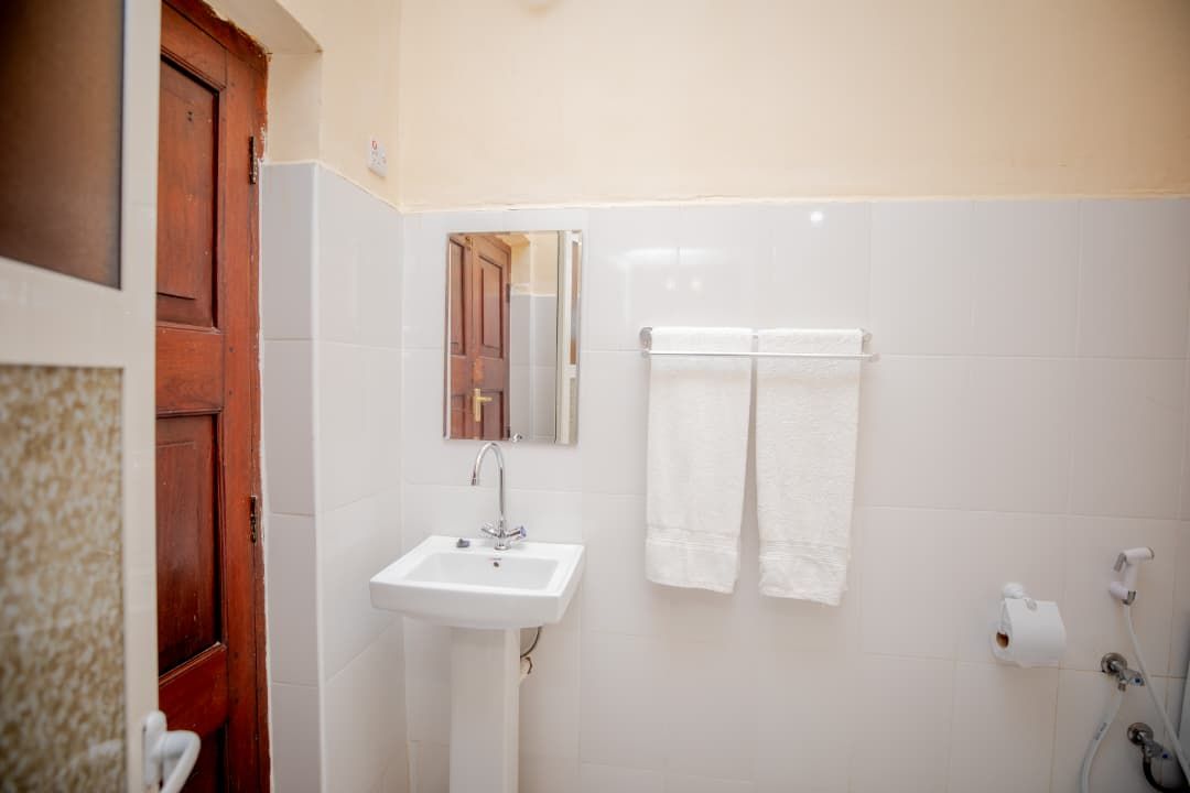 A bathroom with a white sink, a towel rack with two towels, a wooden door, and a mirror.