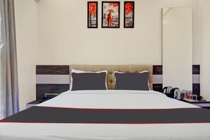 A hotel room with a bed, two pillows, a bedside table with a phone, a coffee maker, and a tray with water bottles.