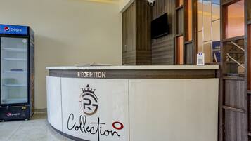 Un mostrador de recepción con un logotipo y la palabra 'Collection', un refrigerador Pepsi y una cámara de seguridad en la pared.