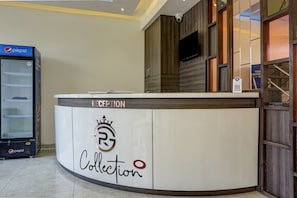 Un taulell de recepció amb un logotip i la paraula 'Collection', un refrigerador de Pepsi i una càmera de seguretat a la paret.