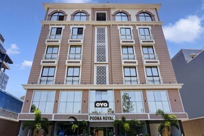 A multi-story hotel with a central vertical decorative panel, balconies with metal railings, and a sign for 'POONA ROYAL' at the ground level.