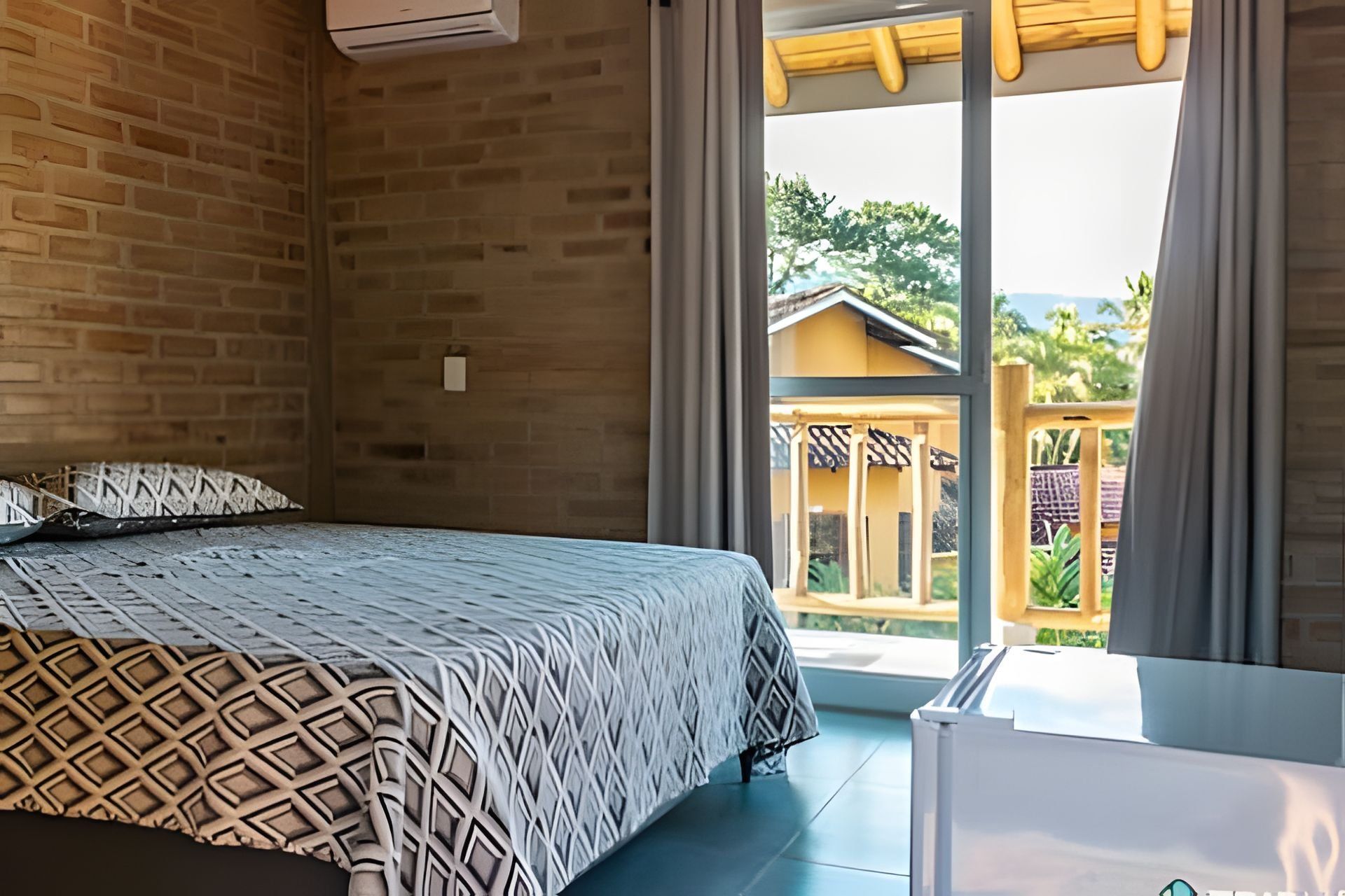 A bedroom with a bed, a brick wall, and a view of a building outside.
