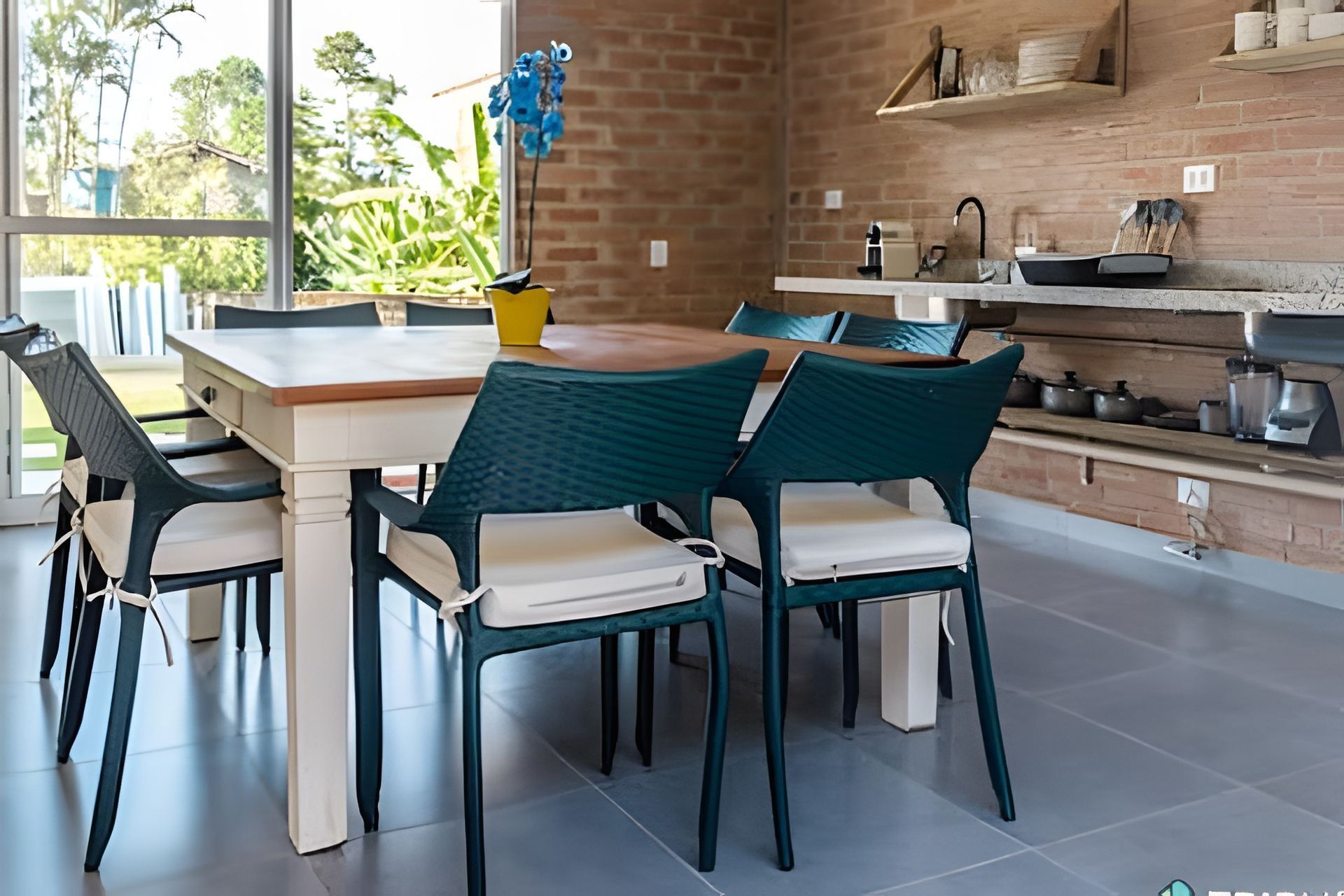 A modern kitchen with a brick wall, a dining table with chairs, and a view of greenery outside.