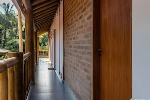 A corridor with wooden railings and a brick wall, leading to a balcony with a view of greenery. - Recanto da Feiticeira (Ilhabela)