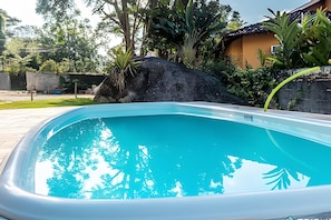 A swimming pool with clear blue water, surrounded by lush greenery and a large rock. - Recanto da Feiticeira (Ilhabela)
