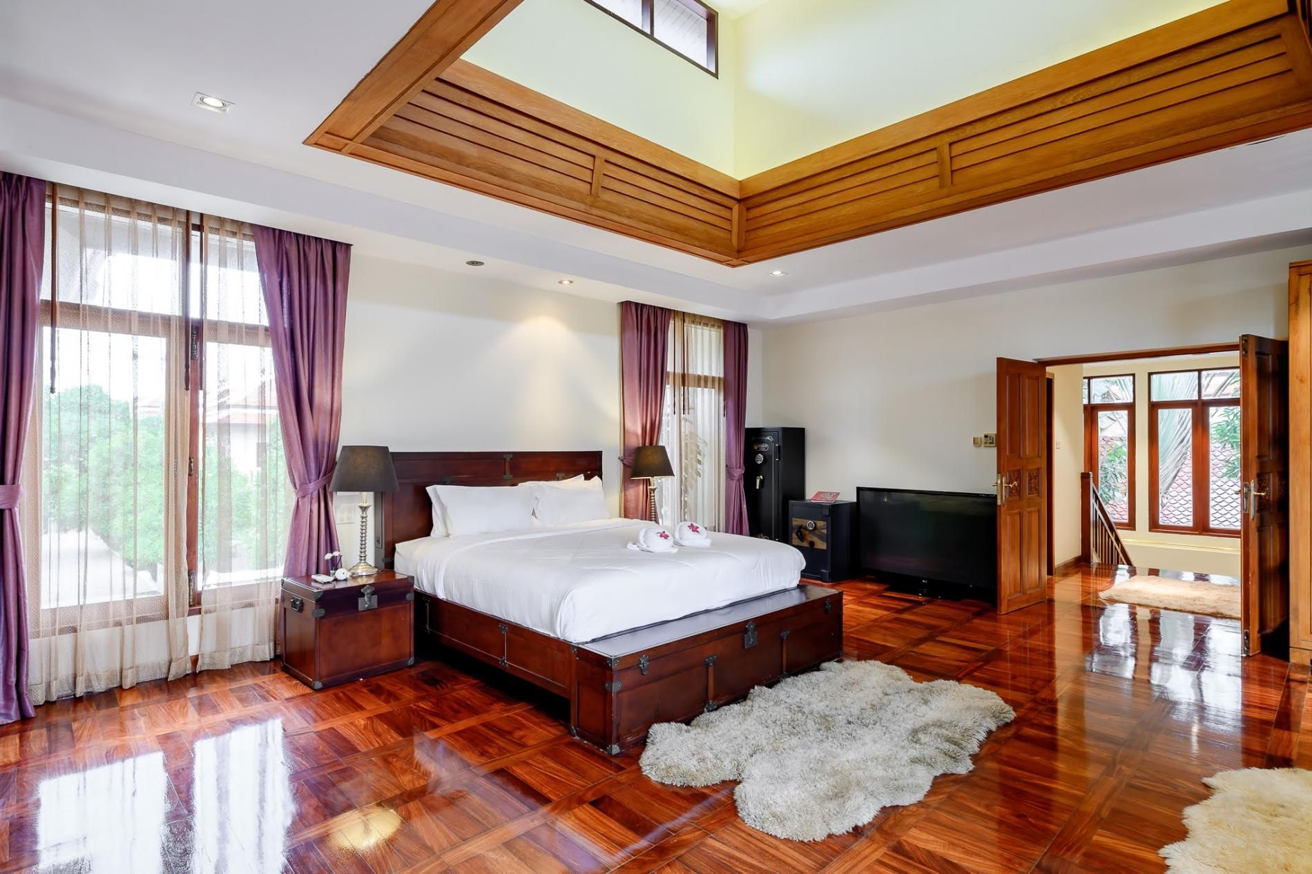 A spacious bedroom with a large bed, wooden flooring, a television, and a wardrobe.