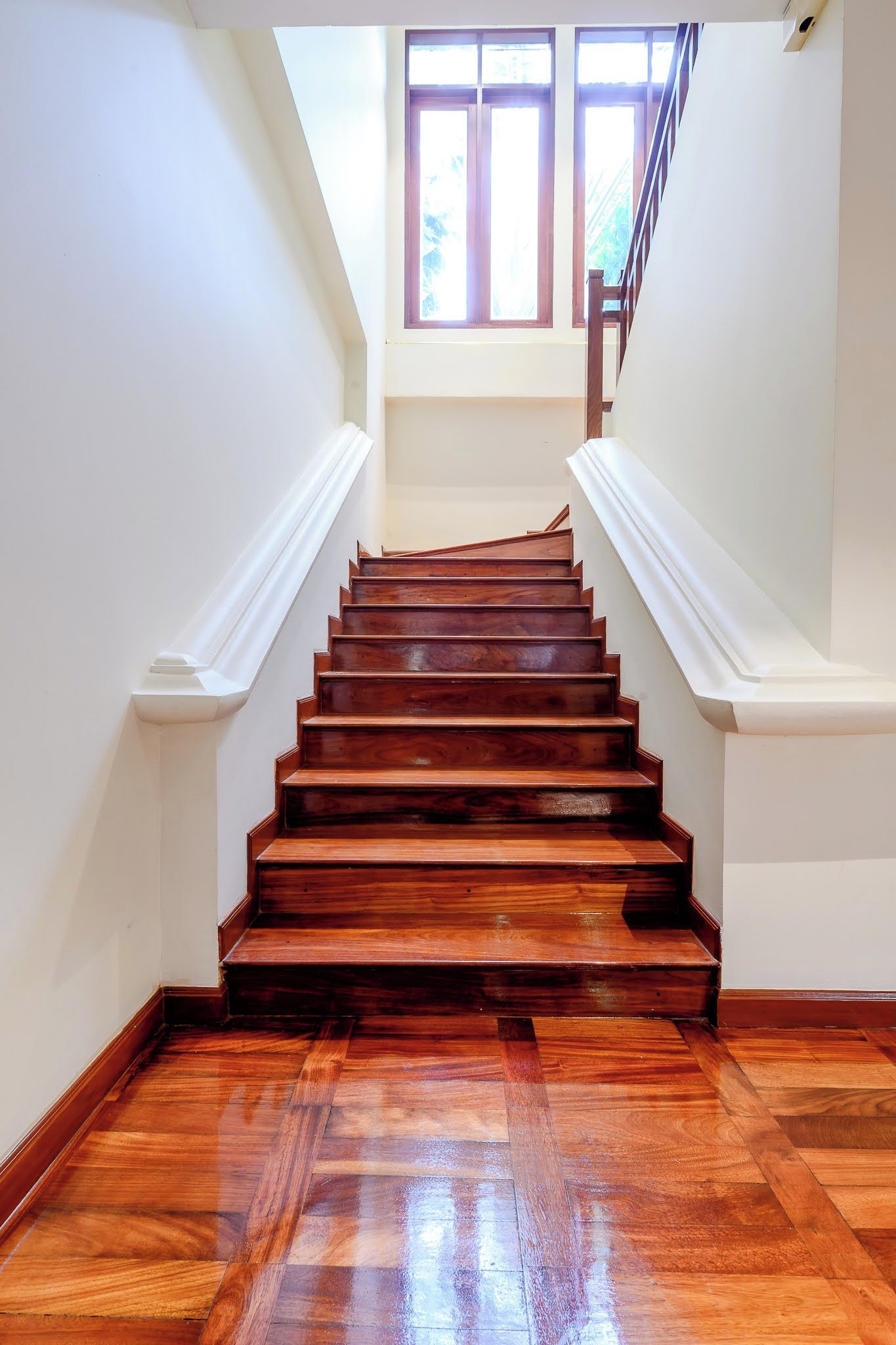 Una scala in legno con stipiti bianchi che porta a un pianerottolo con finestre.