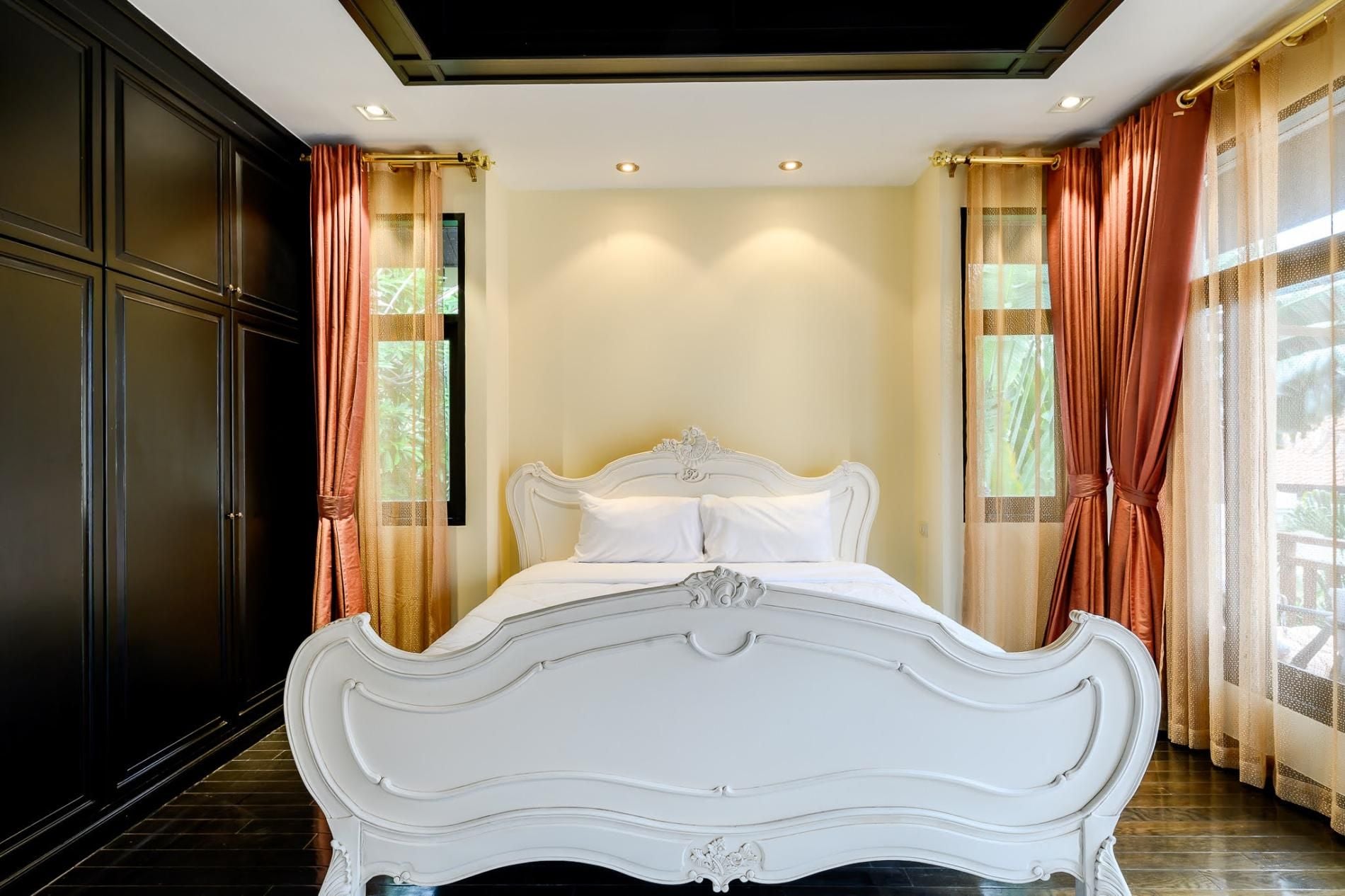Une chambre à coucher avec un lit blanc à baldaquin, une armoire en bois foncé et des rideaux vaporeux.