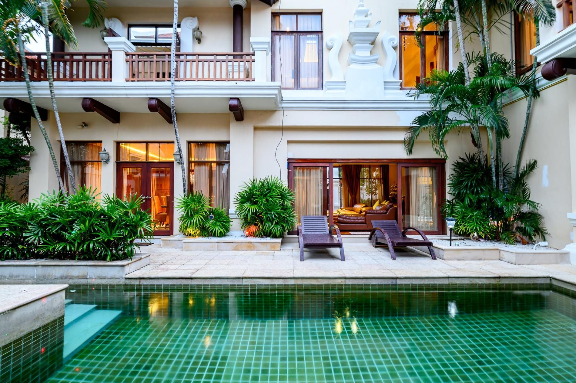 A hotel with a pool, outdoor seating, and tropical plants.