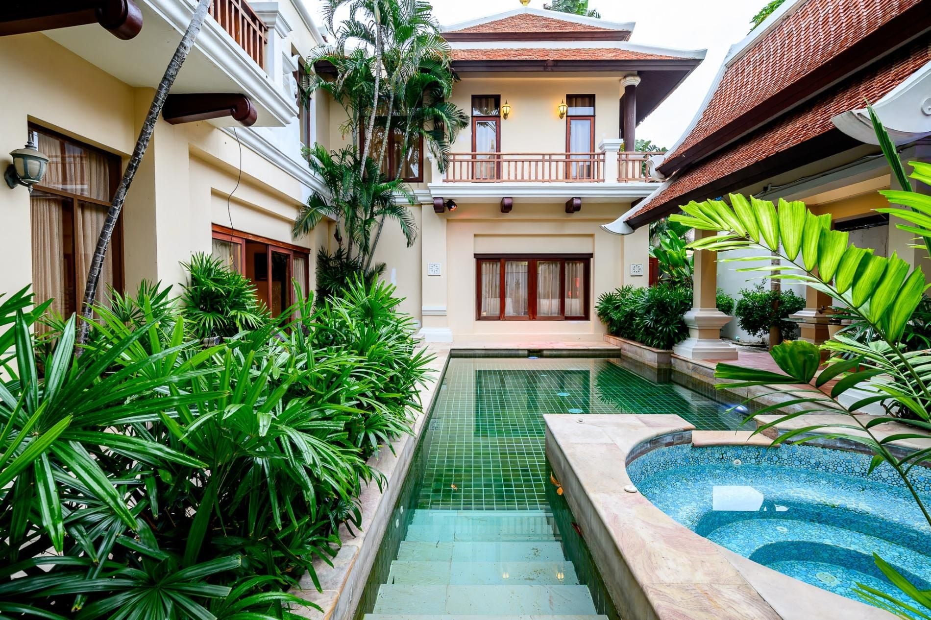 Une cour avec une piscine, entourée d’une végétation luxuriante et bordée d’édifices à l’architecture traditionnelle.