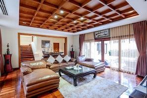 Un salón espacioso con techo de madera, sofás de cuero, una mesa de centro de vidrio y un gran ventanal con cortinas.