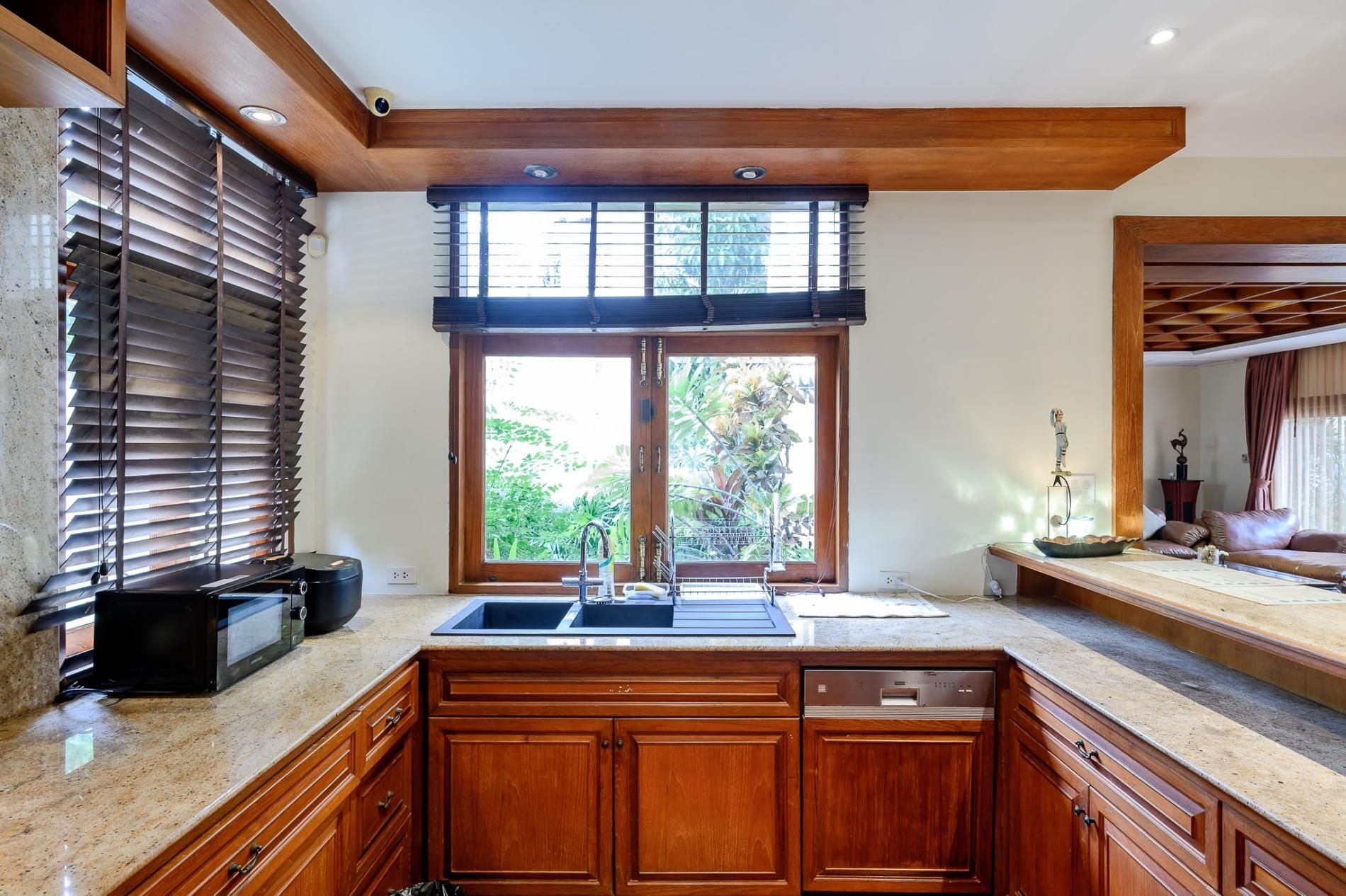 A kitchen with wooden cabinets, a double sink, and a window with blinds.